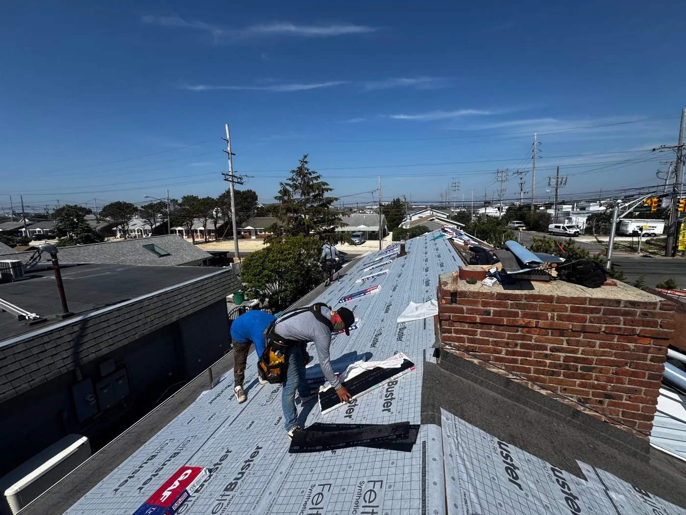 Roofers working on the shingles next to a brick chimney