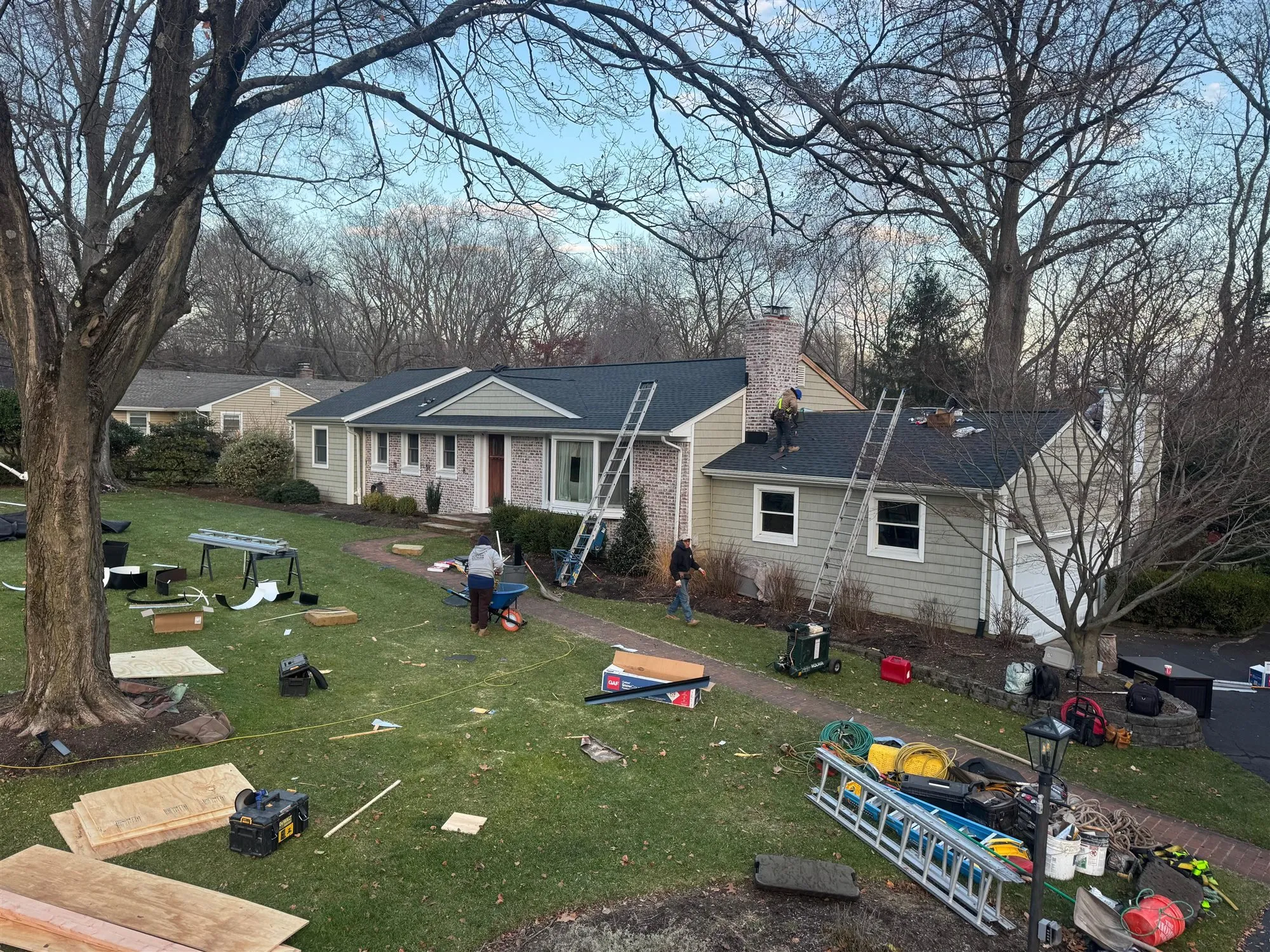 Imperial roofers re-roofing a brick and siding ranch house, with materials staged on the lawn