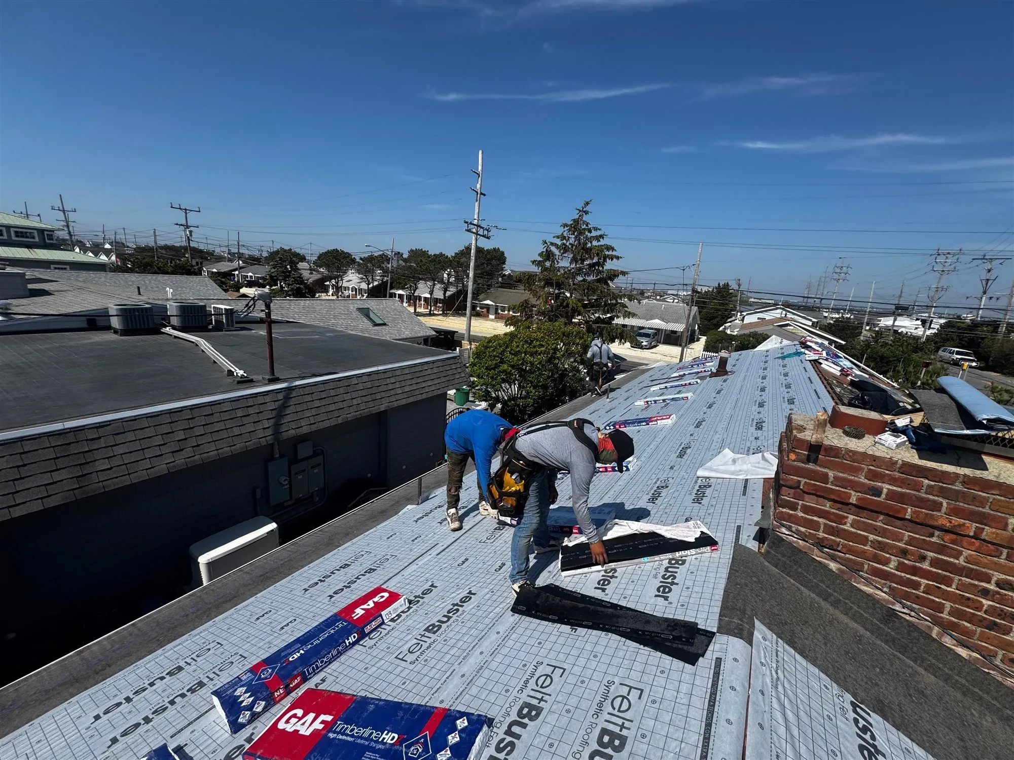 Roofer installing synthetic underlayment next to a brick chimney