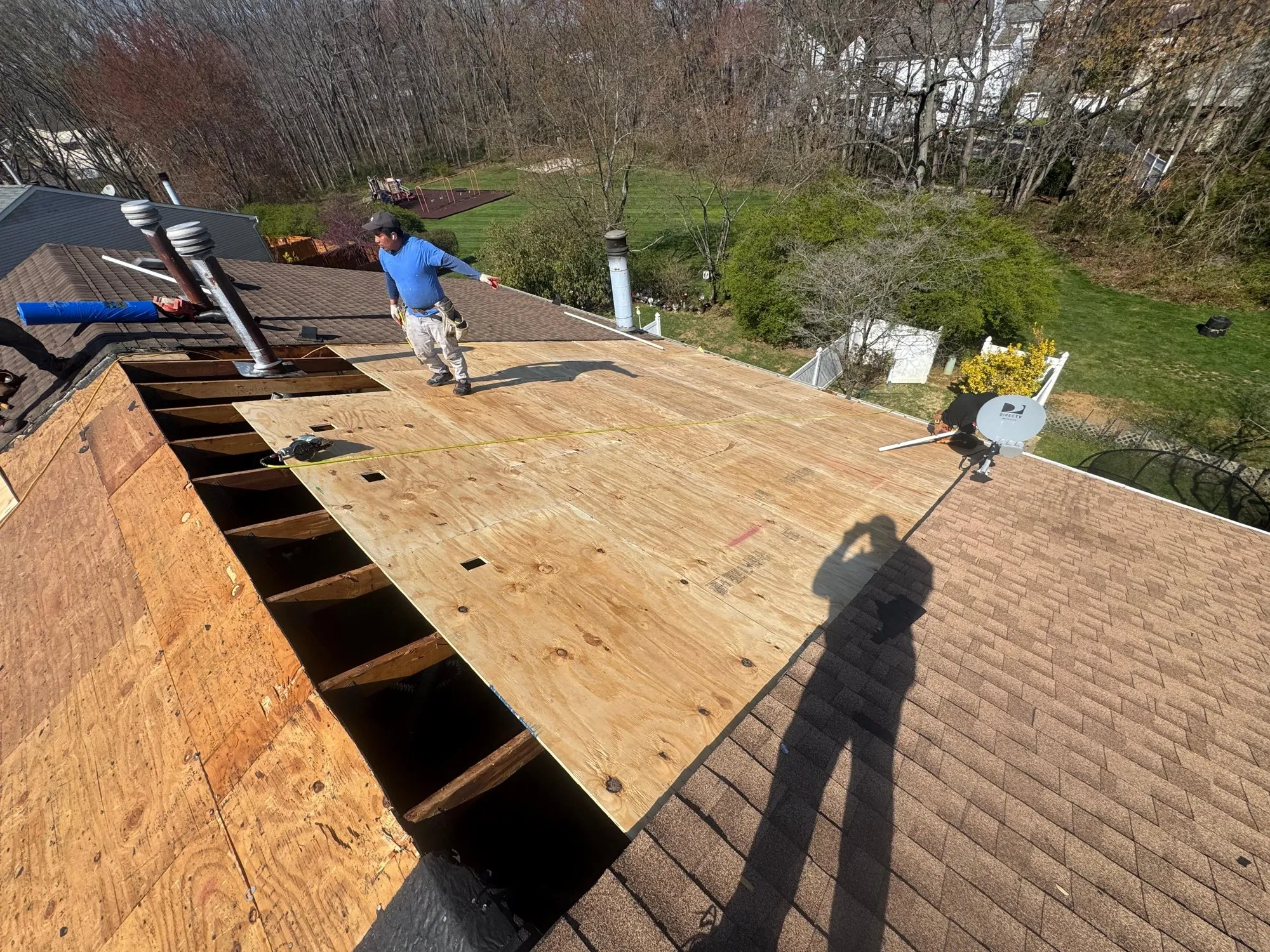 Damaged roof decking cut out and new plywood sheets going down over the rafters during a tear-off