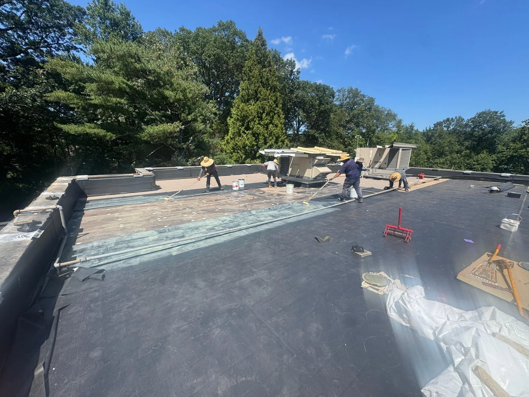 Crew installing a new flat roof membrane section by section