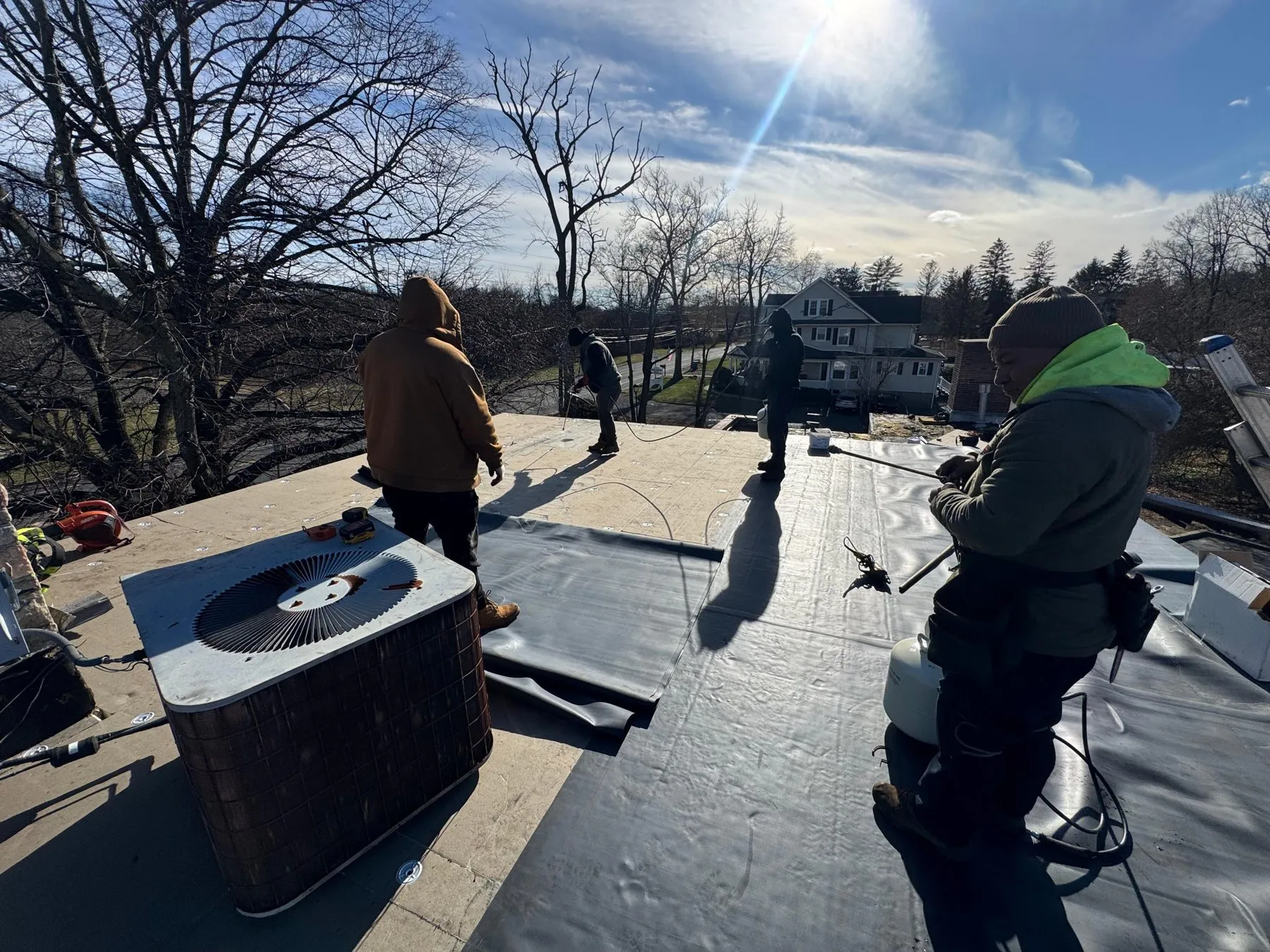 Roofers installing a new flat roof membrane around a rooftop unit