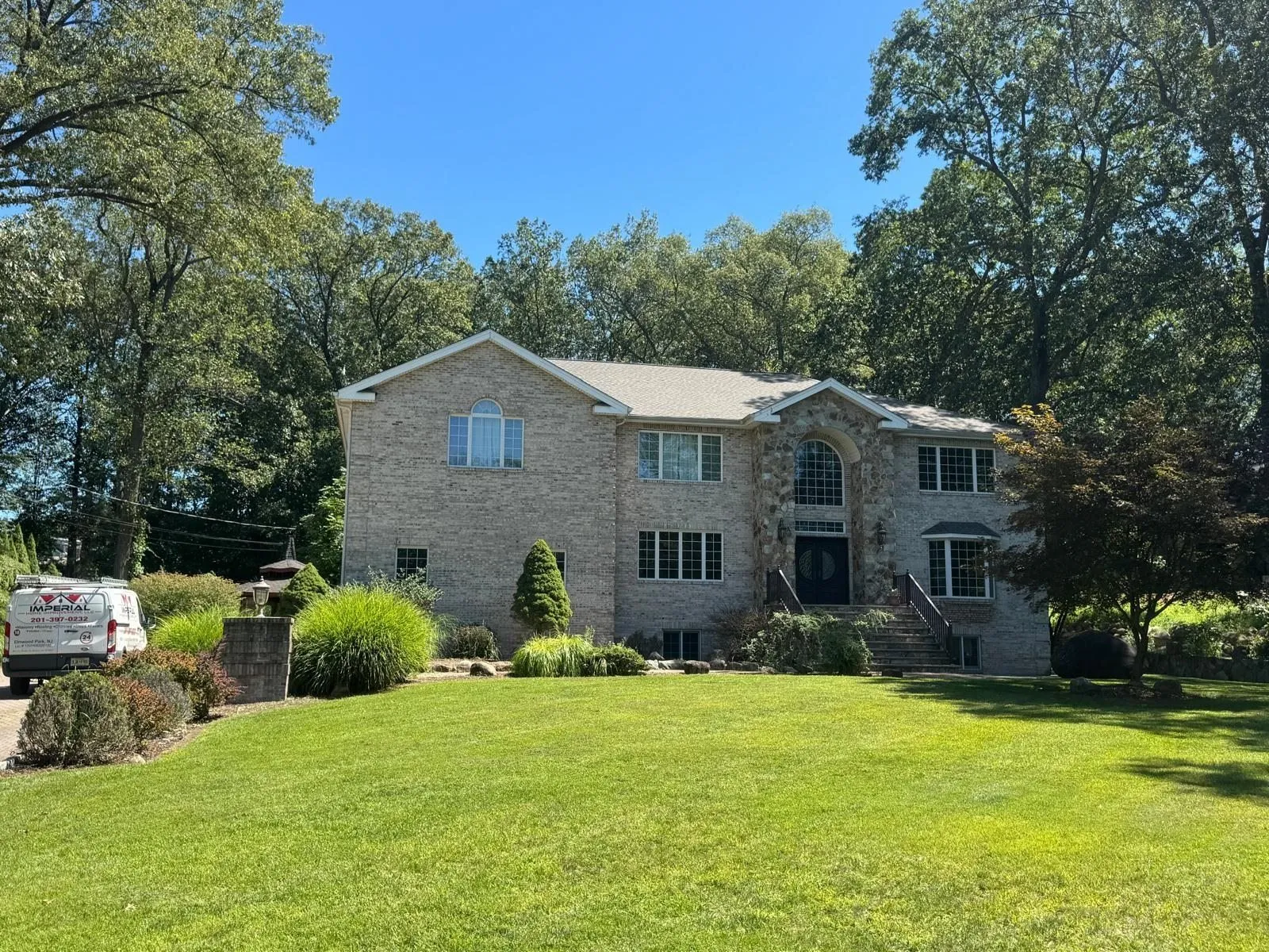 Brick two-story house with a new roof, surrounded by trees