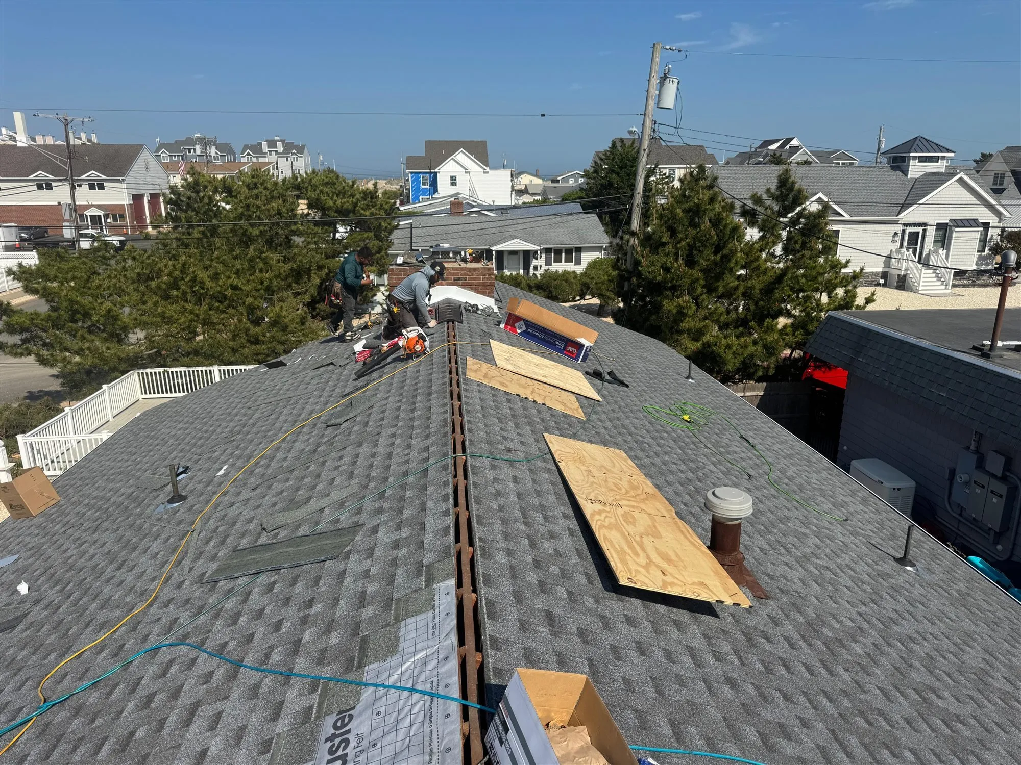 Roofers installing architectural shingles over new plywood decking during a roof replacement