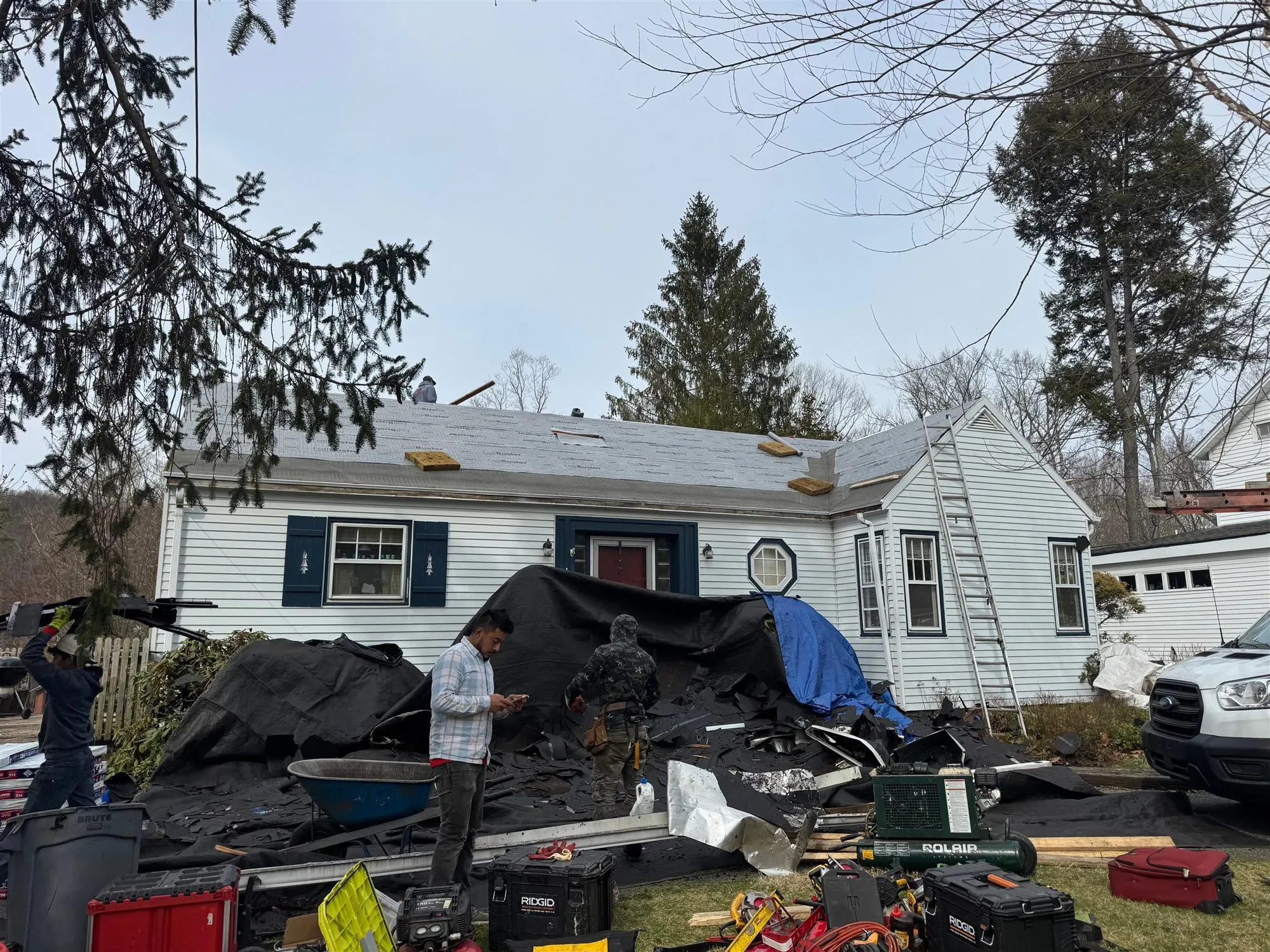 Old roofing debris and tarps in front of a house during a tear-off